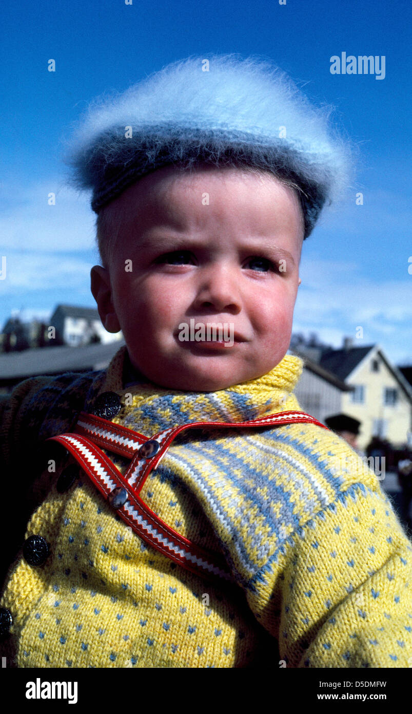 A cute Norwegian baby boy wearing a Nordic woolen sweater and furry hat faces the bright winter