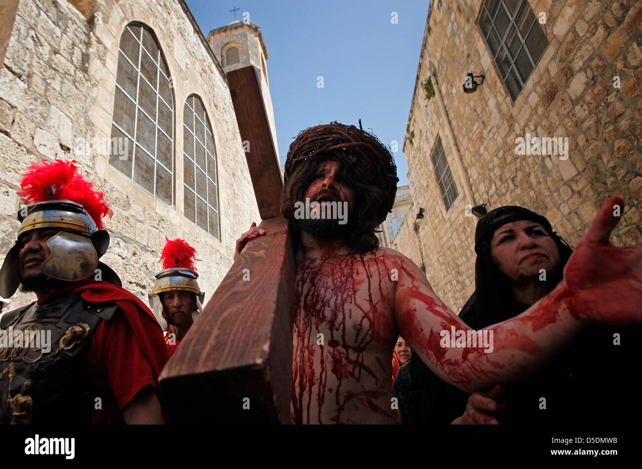 A Christian devotee dressed as Jesus Christ carries a wooden cross reenacting the Stations of the Cross during Good Friday procession along Via Dolorosa street believed to be the path that Jesus walked on the way to his crucifixion in the Old City East Jerusalem, Israel Stock Photo