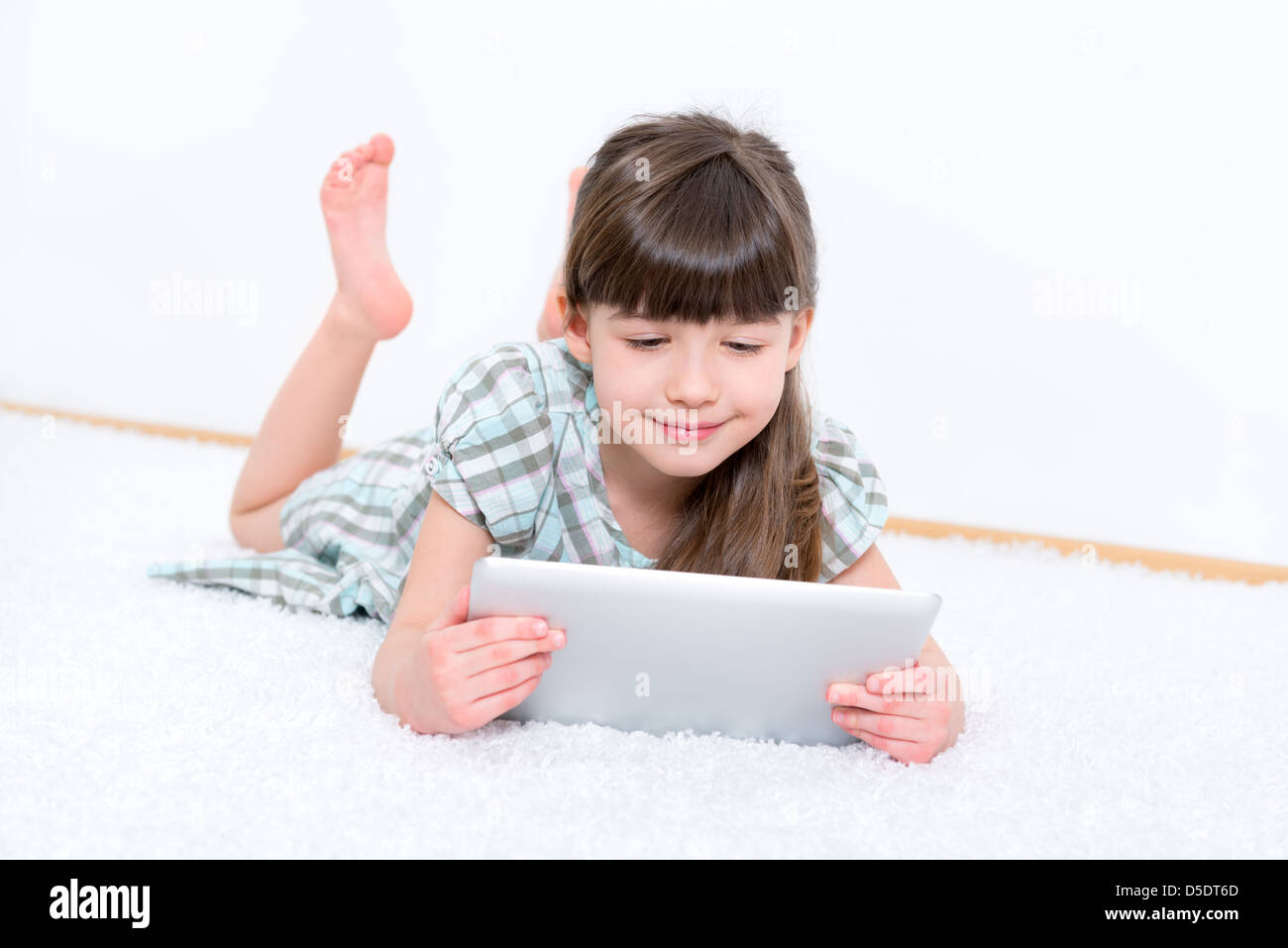 Young girl (6-7 year) looking and playing with digital tablet in a white room. Stock Photo