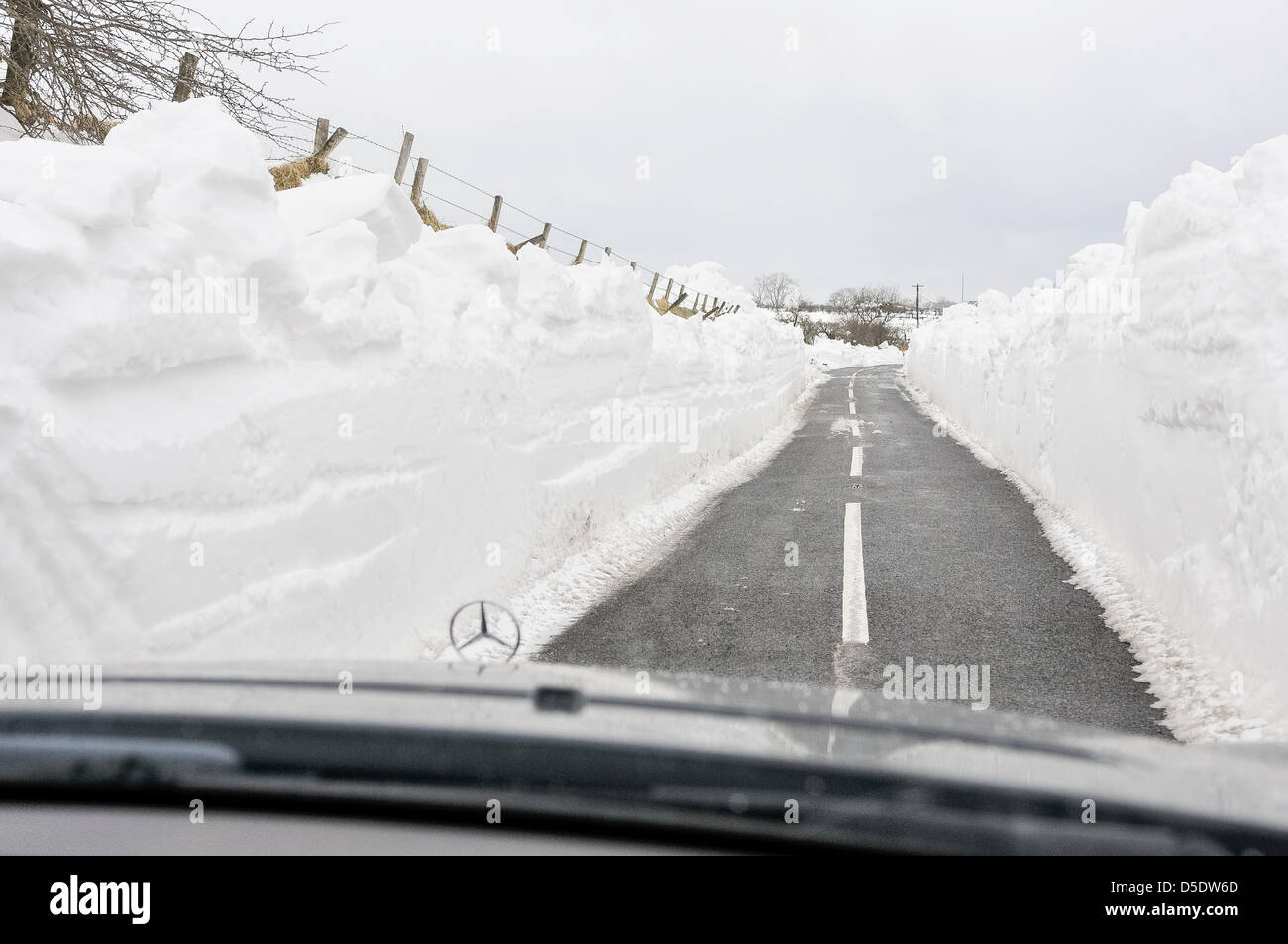 Carrickfergus, Northern Ireland. 29th March, 2013. A Mercedes car drives between deep walls of snow which line a recently cleared rural road Stock Photo