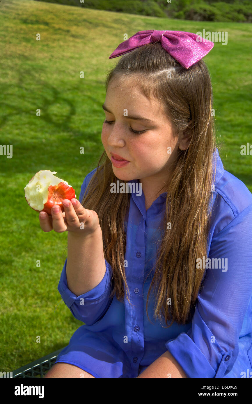 A happy young Caucasian girl eats a Gala apple outdoors in a Lagnua Beach, CA, park. Stock Photo