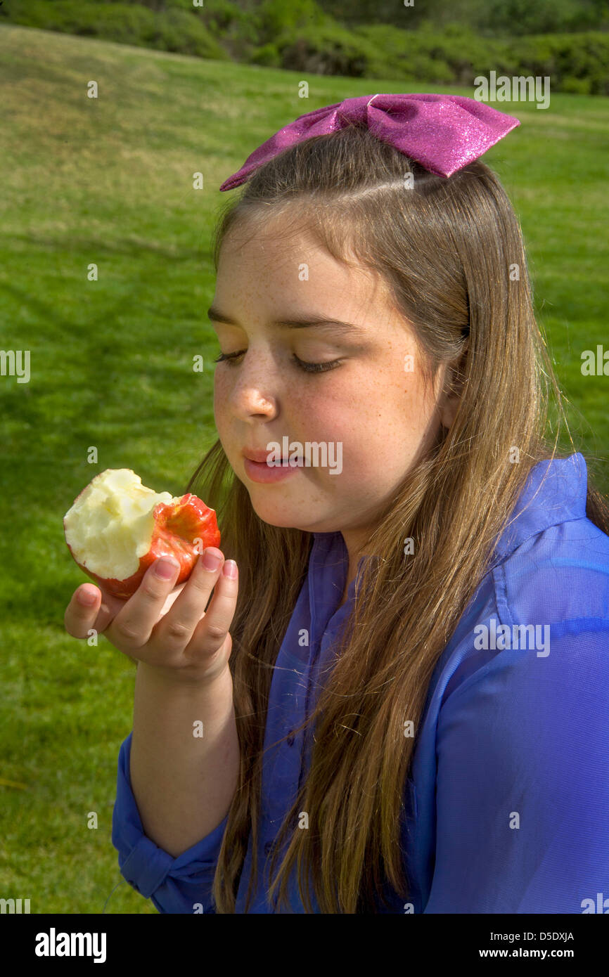A happy young Caucasian girl eats a Gala apple outdoors in a Lagnua Beach, CA, park. Stock Photo