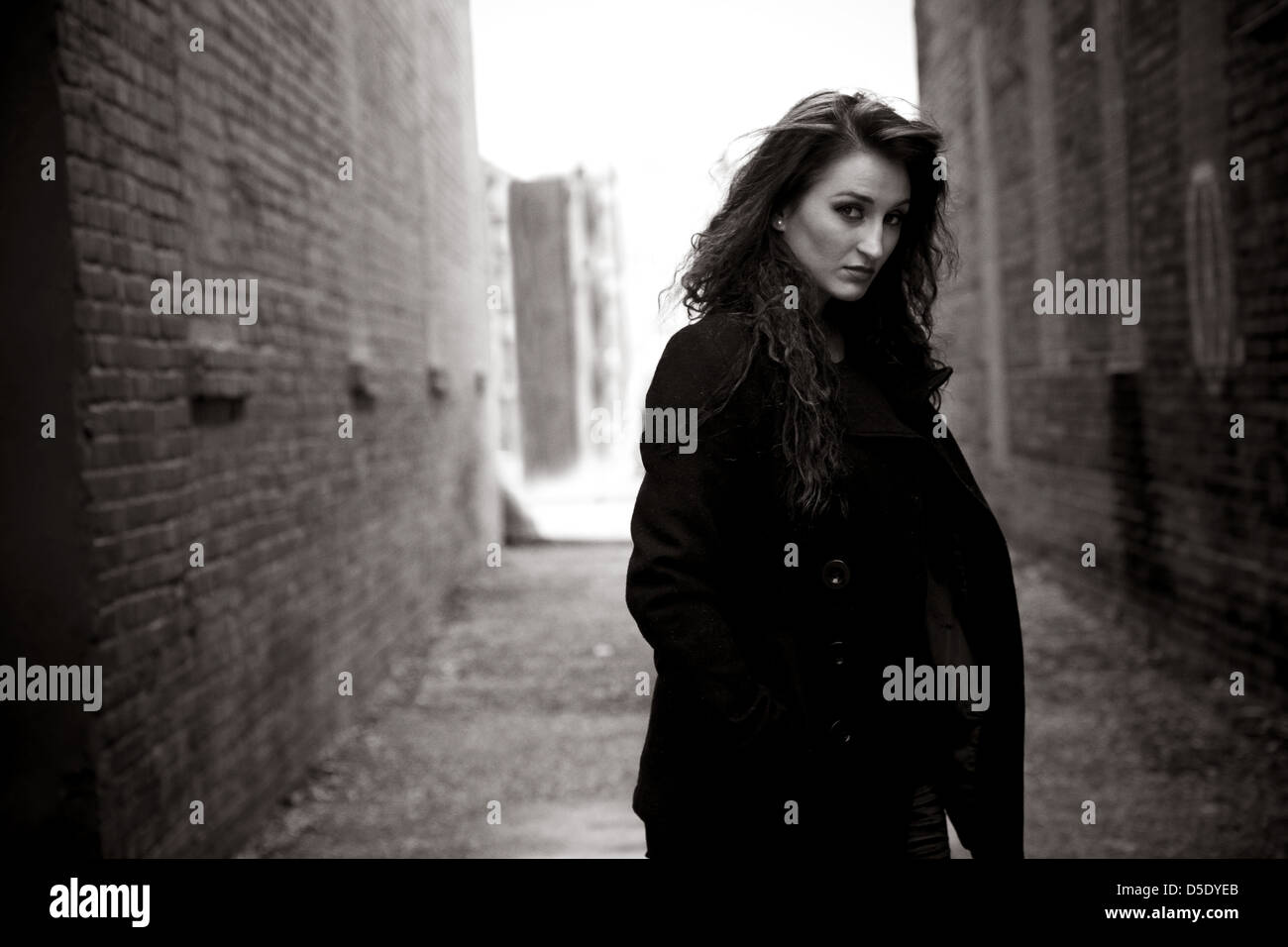 Woman in dark clothes rainy day in alley Stock Photo
