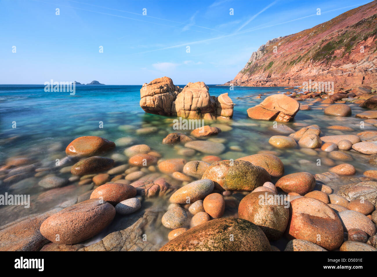 Boulders on Porth Nanven cove with Bubble Gum Rock and The Brisons in the distance.  Captured using a long shutter speed. Stock Photo