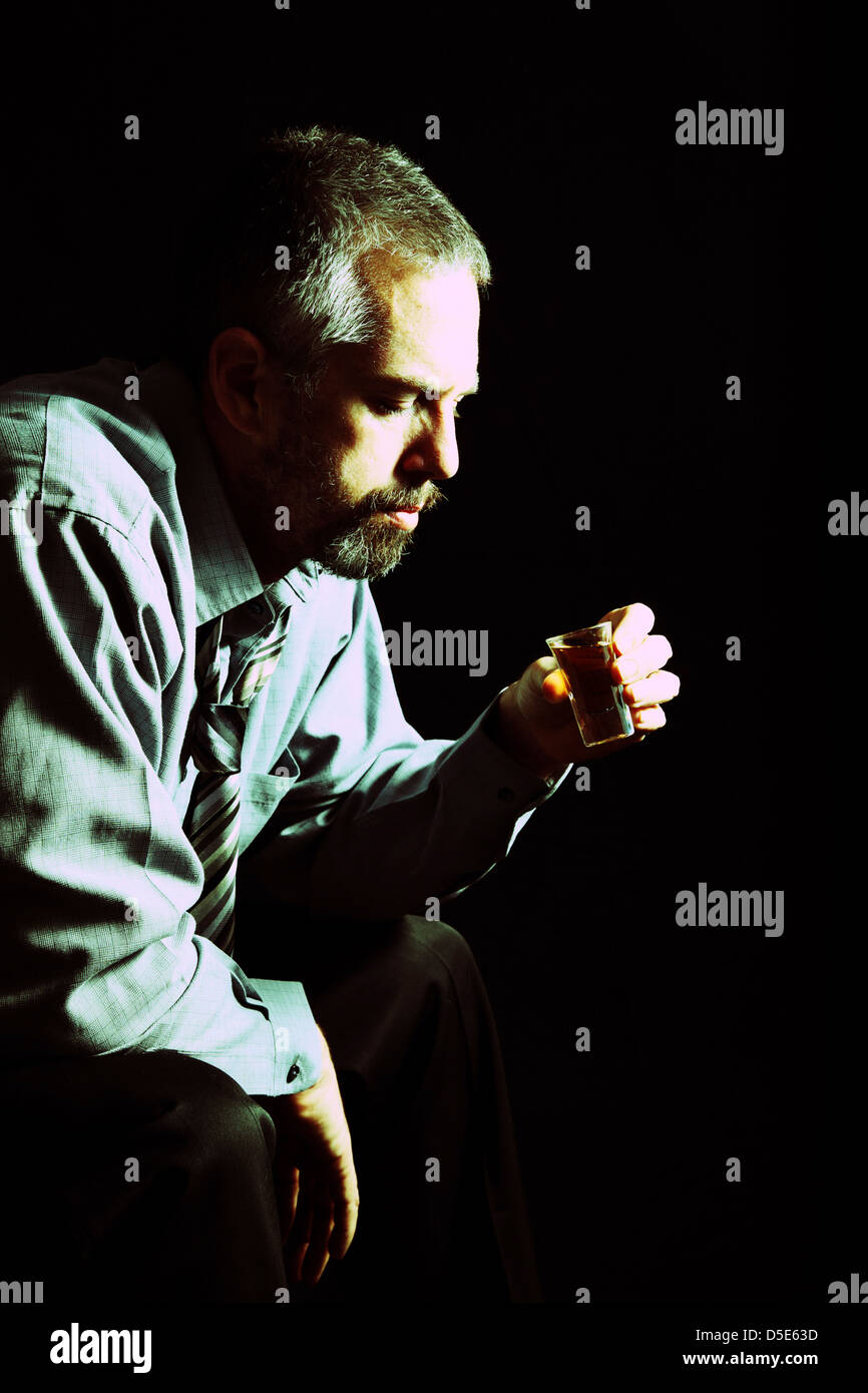 Low key portrait of business man thinking about taking another drink of alcohol. Stock Photo