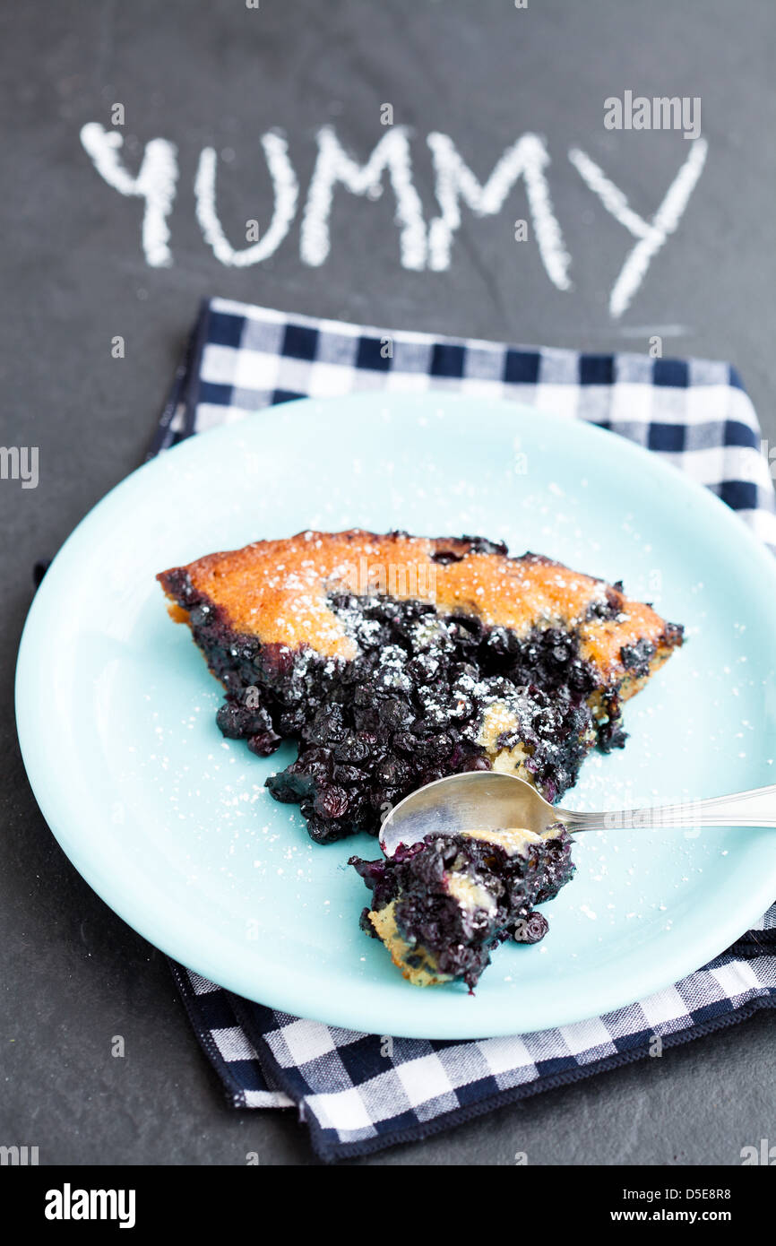 Closeup of slice of delicious blueberry pie on plate with spoon on dark surface with word yummy written in chalk Stock Photo