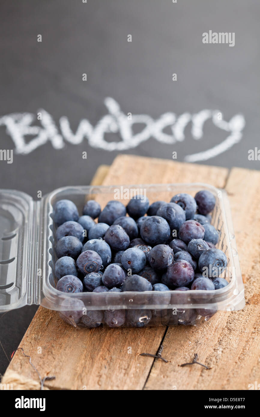 Fresh blueberries in plastic container on wooden serving surface with