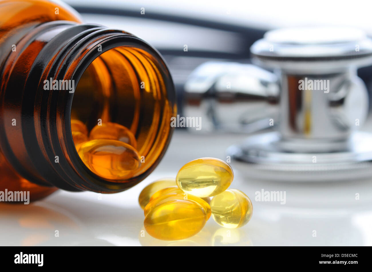 Closeup of a pill bottle on its side with capsules spilling out. An out of focus stethoscope is