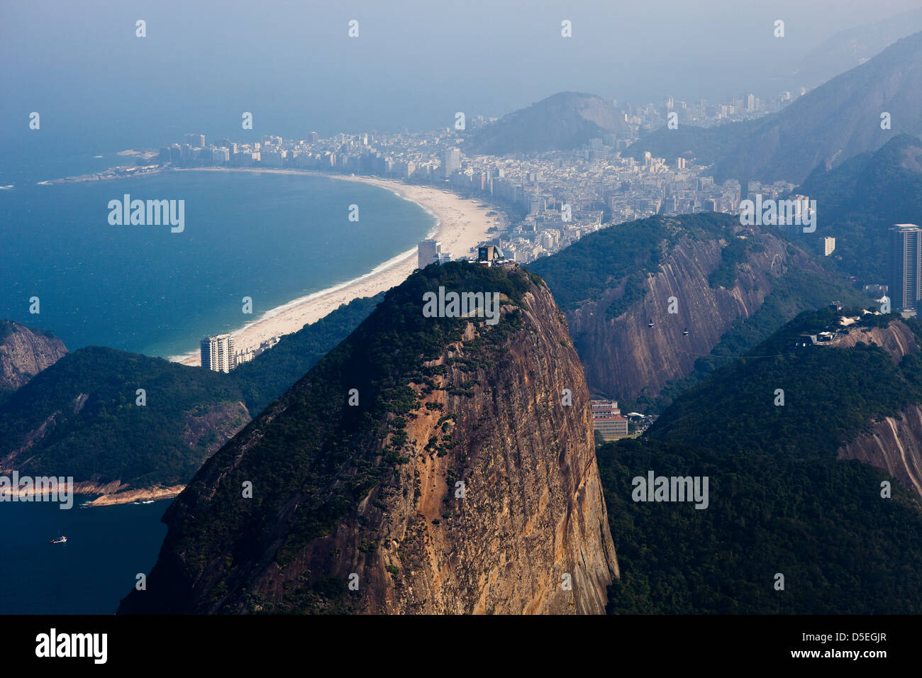Top of Sugar Loaf mountain in the foreground and Copacabana beach and neighborhood in the background on a misty and hot summer morning - high humidity Stock Photo