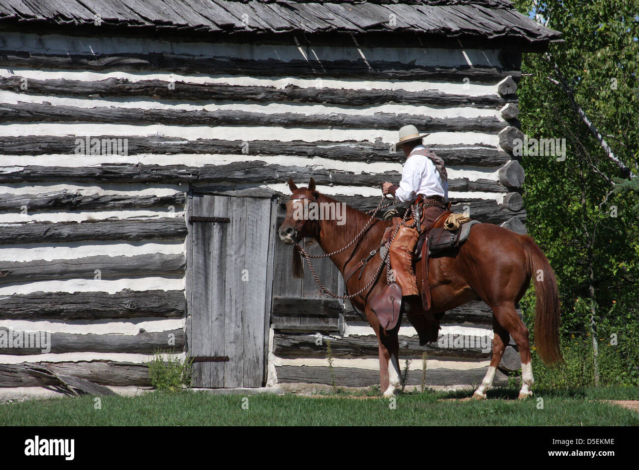 A cowboy and horse next to a log cabin Stock Photo
