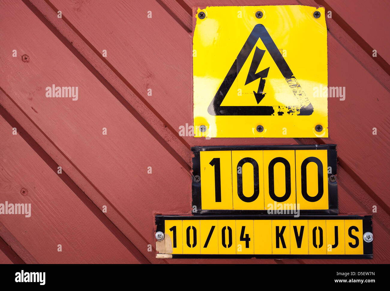 Yellow high voltage caution sign on red wooden wall Stock Photo