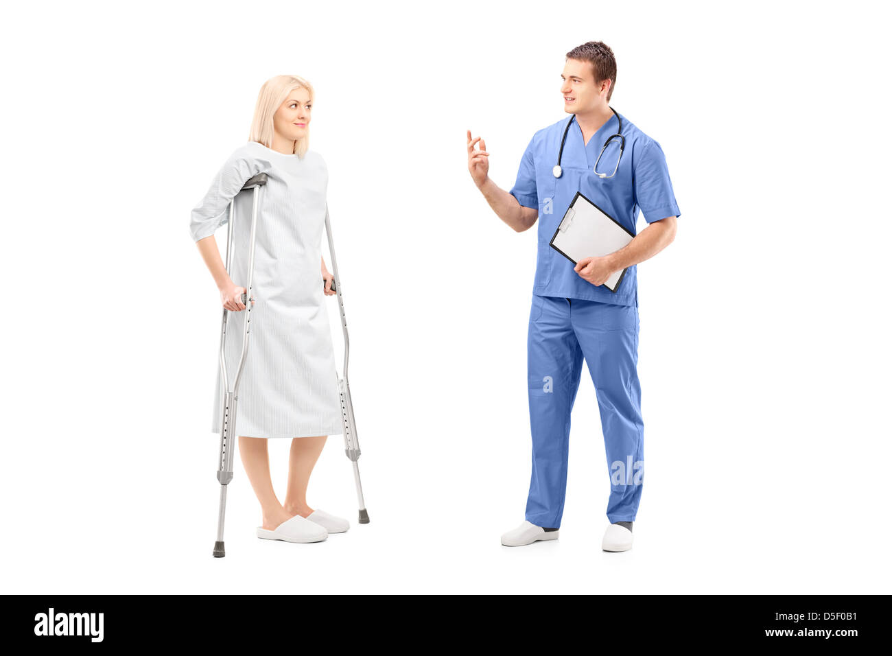 Full length portrait of a blond female patient in hospital gown with crutches and medical practitioner during a conversation Stock Photo