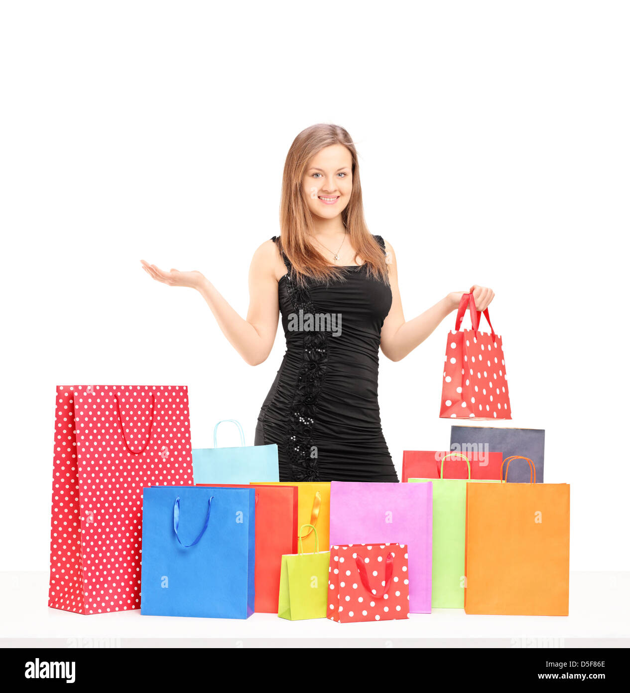 Beautiful young female holding a present and posing with shopping bags on a table isolated on white background Stock Photo
