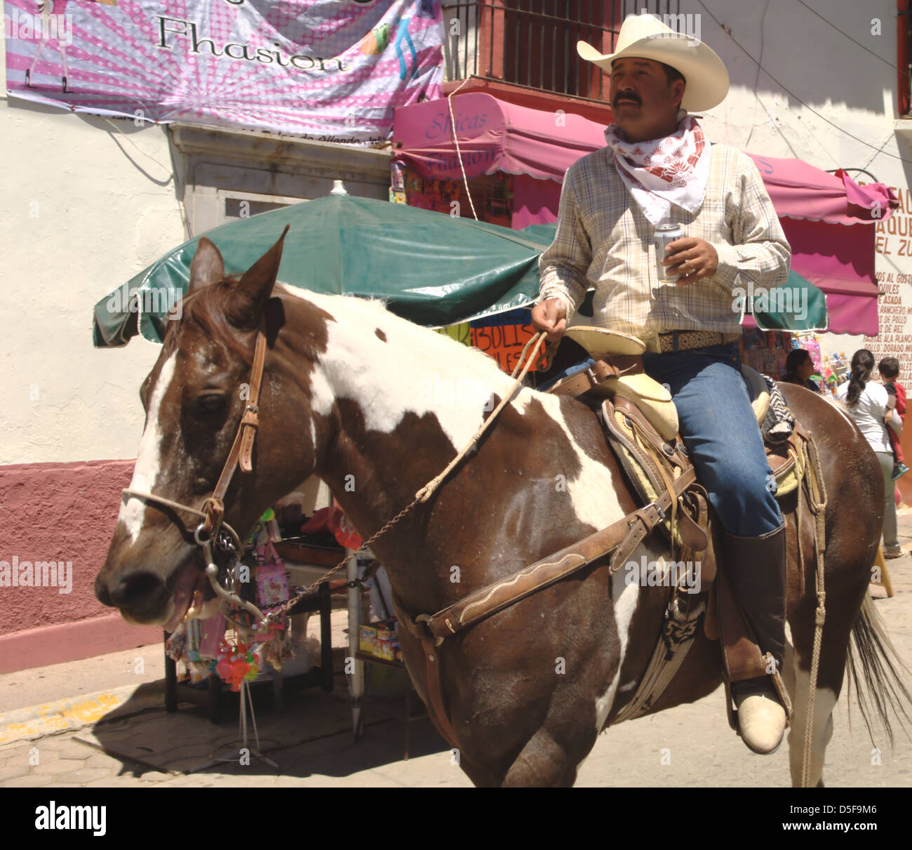 Vaquero drinking beer whilst riding his horse. Stock Photo