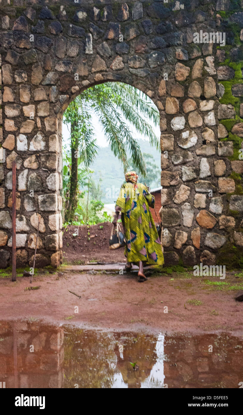African woman walking with cane in colourful dress out a stone church archway in Cameroon Stock Photo