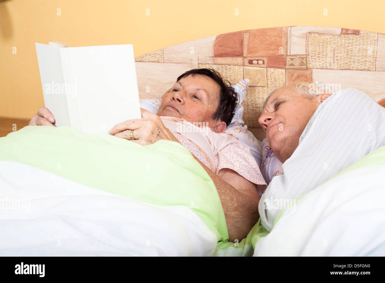 Close up of two seniors reading book in bed. Stock Photo