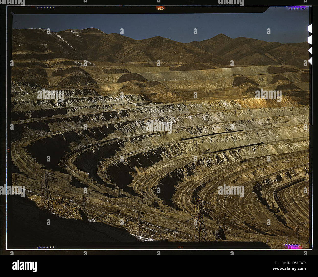 This photograph from the 1940s captures the open-pit mining operations at the Utah Copper Company's site in Carr Fork, Bingham Canyon. The massive pit, with power lines running across, illustrates the scale of copper extraction and mining techniques during the era. Stock Photo
