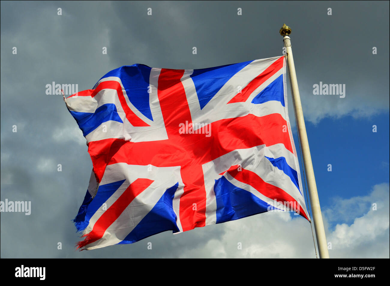 UNION JACK FLAG FLYING IN THE WIND WITH DRAMATIC SKY BEHIND Stock Photo