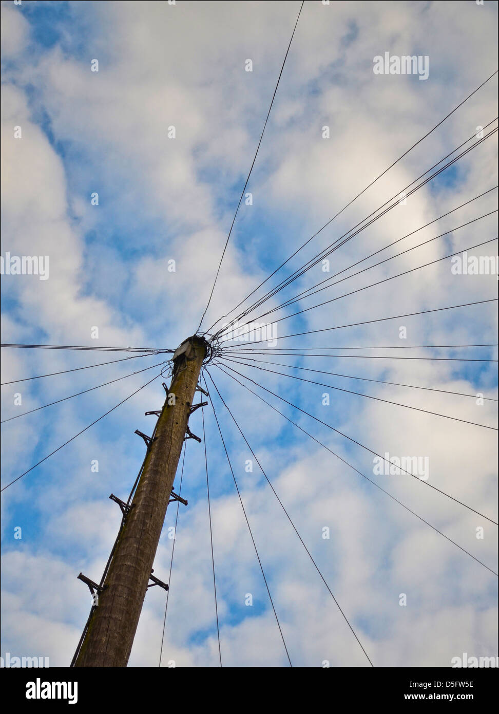 OLD FASHIONED TELEPHONE POLE WITH LINES RUNNING TO HOUSES AND CLIMBING STEPS AGAINST A BLUE SKY Stock Photo