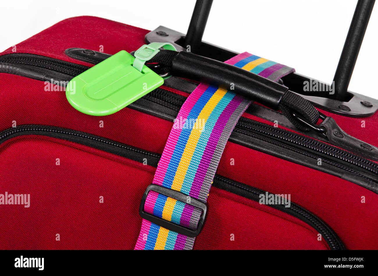Closeup of bright green luggage tag and colorful belt on red suitcase Stock Photo