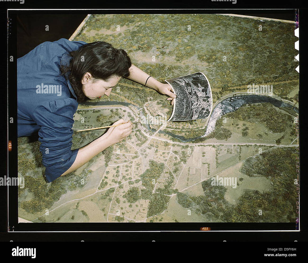 Camouflage class at N[ew] Y[ork] University, where men and women are preparing for jobs in the Army or in industry, New York, N.Y. This model has been camouflaged and photographed. The girl is correcting oversights detected in the camouflaging of a model Stock Photo
