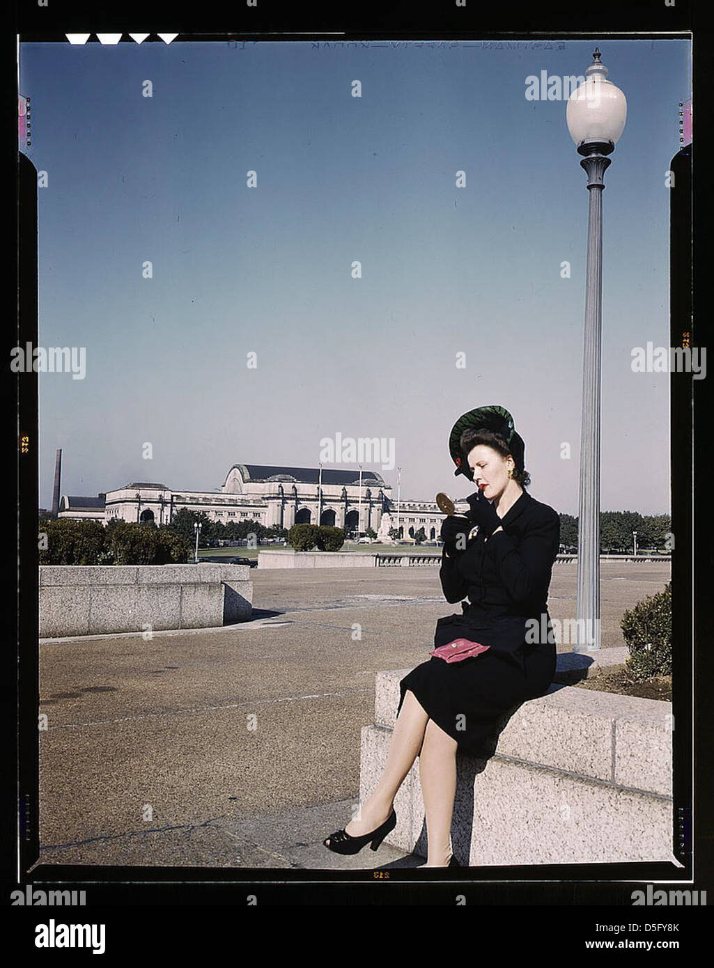 Woman putting on her lipstick in a park with Union Station behind her, Washington, D.C. (LOC) Stock Photo