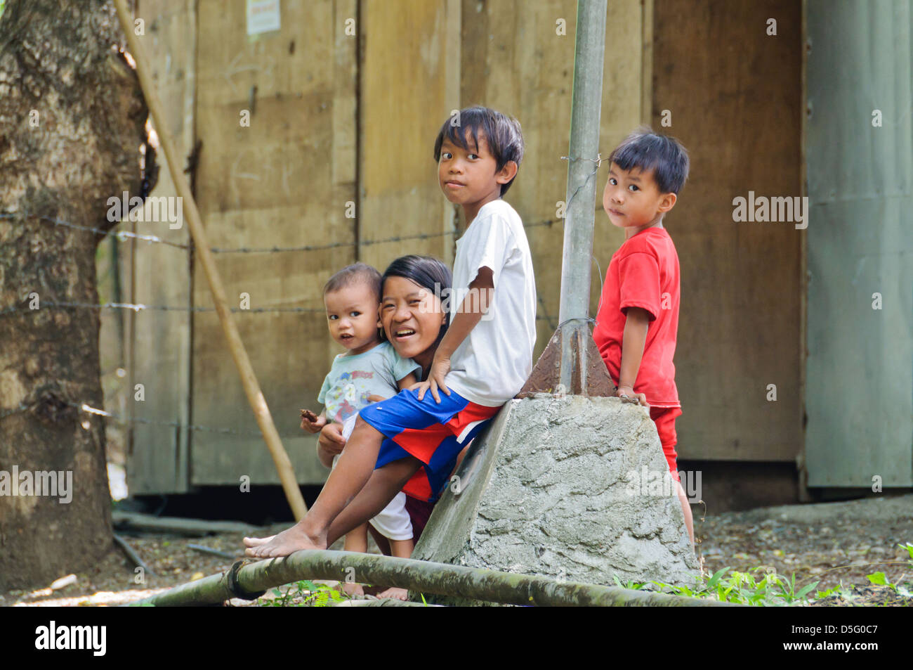 Asian mother with three little children, sitting in front of their poor rural home - Sabang, Puerto Galera, Philippines, Asia Stock Photo