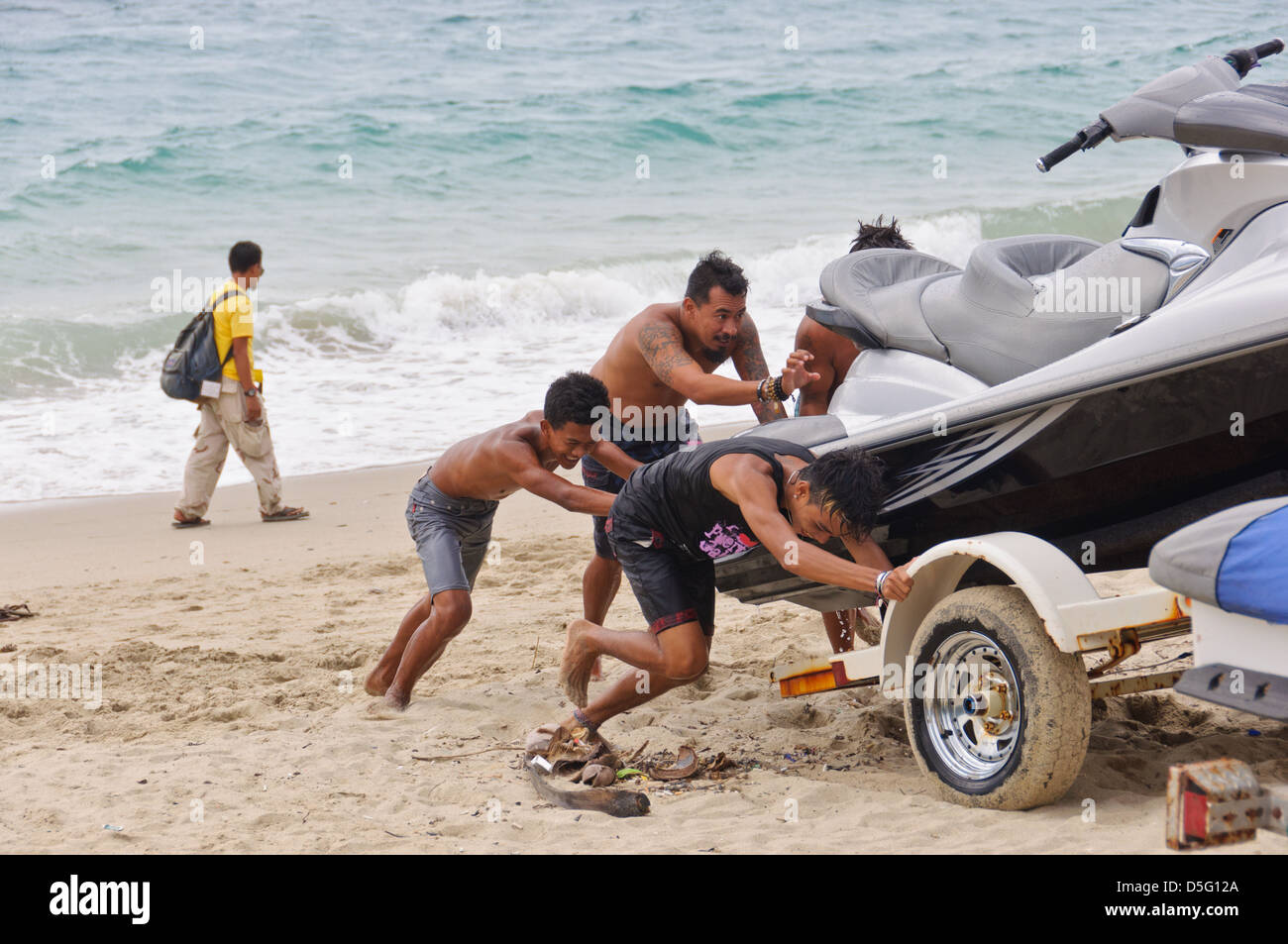 Group of 4 people pulling a jetski out of the ocean on a boat trailer