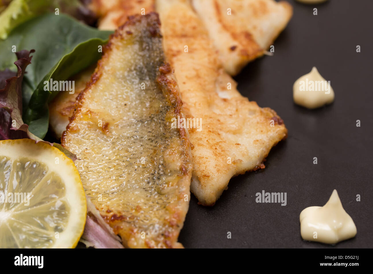 Fried perch fillets with potatoes, lemon and salad in a black plate Stock Photo