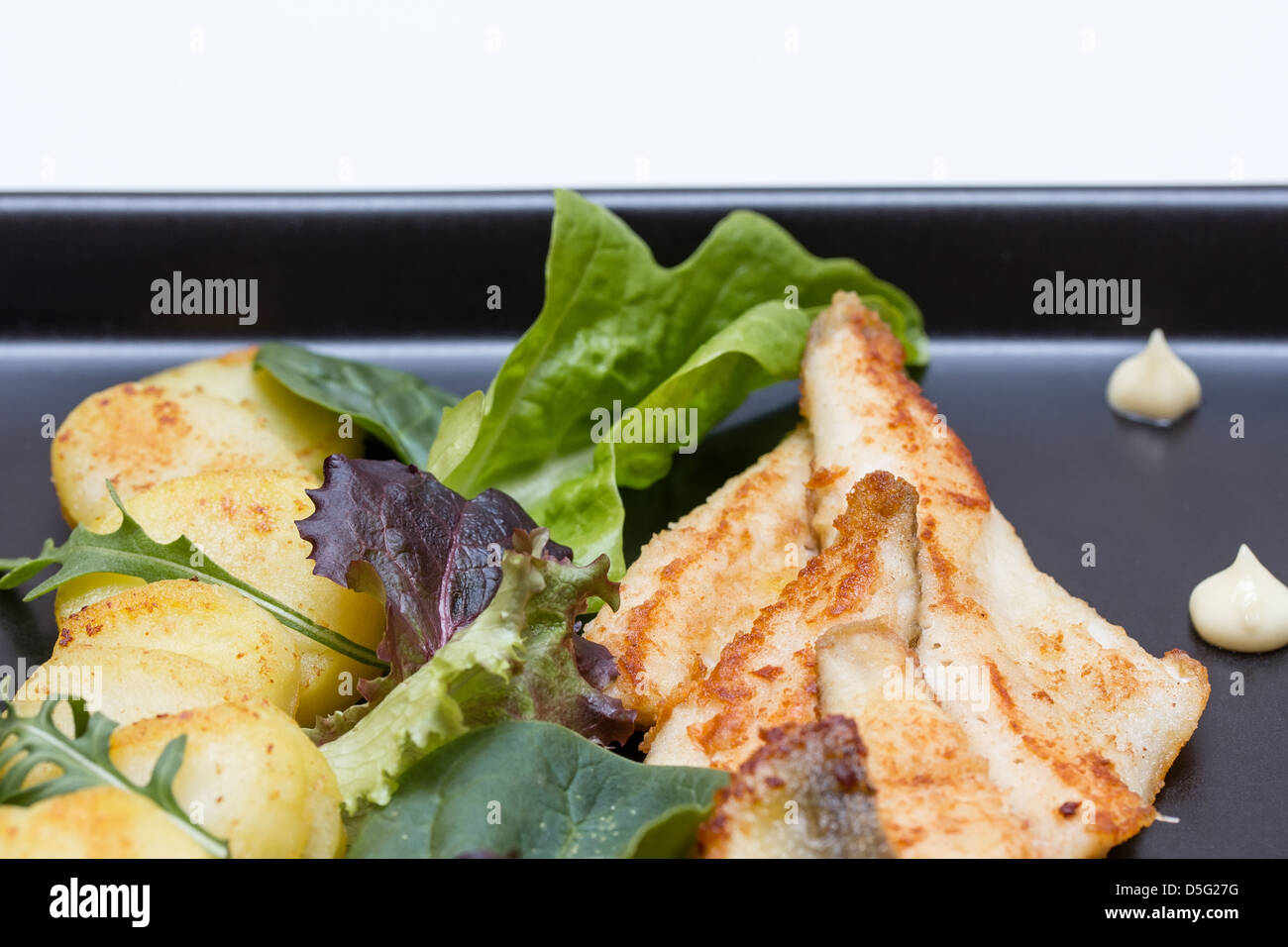 Fried perch fillets with potatoes, lemon and salad in a black plate Stock Photo