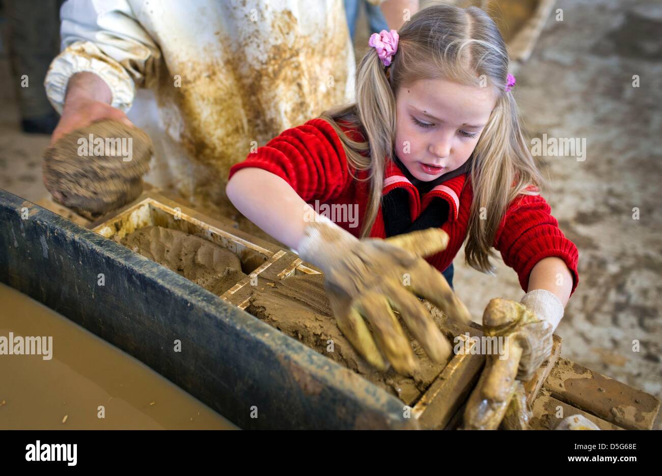 Six year old Lone from Berlin presses clay into wooden brick molds at the brick manufacture in Benzin, Germany, 26 March 2013. The more than 100 year old plant has been restaured in recent years and now prodcues bricks, sheets and plasters from clay according to old techniques. As a living museum it informs visitors about the traditions of once more than 400 brickyards in Mecklenburg. Photo: Jens Buettner Stock Photo