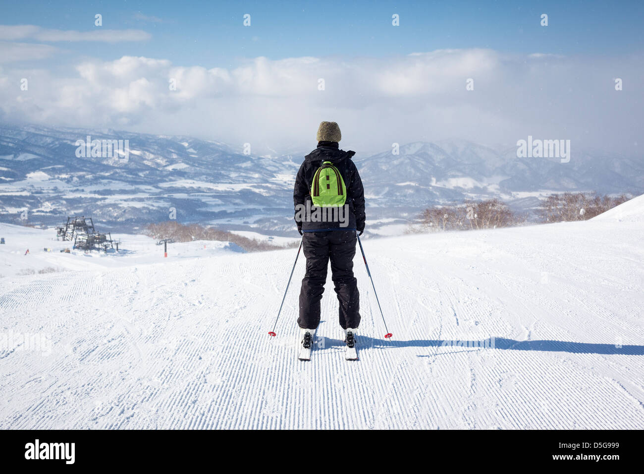 Back view of a female skier as she sets off down a freshly groomed ski slope in the light snow. Stock Photo
