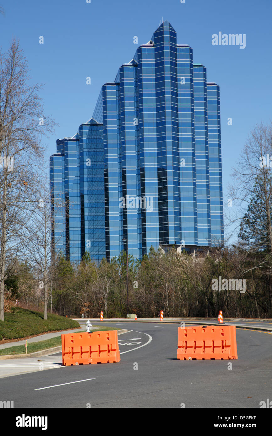 Orange traffic barriers in road in front of blue glass office tower Stock Photo