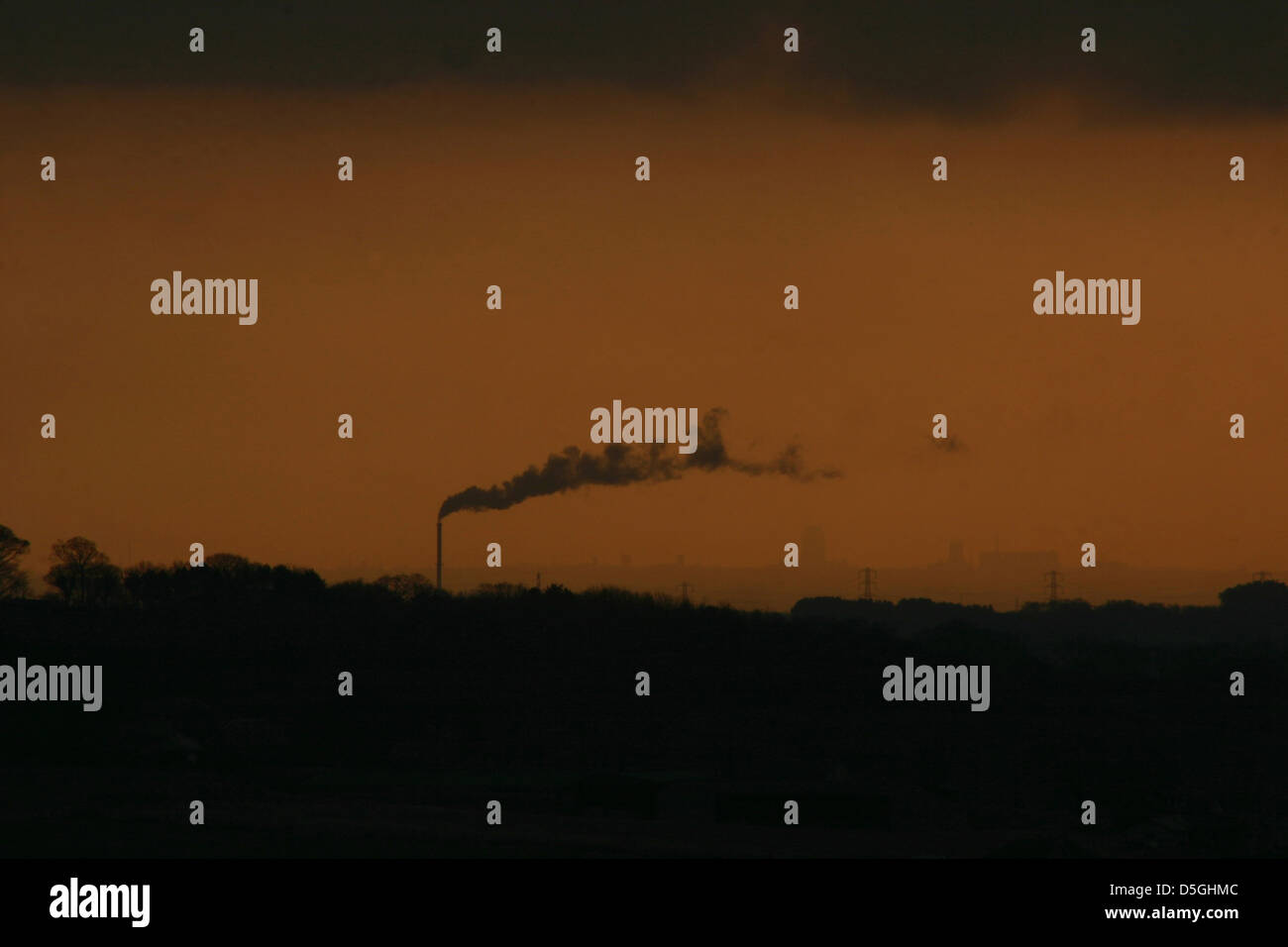 A factory Chimney lays a trail of smoke into dusk. Stock Photo