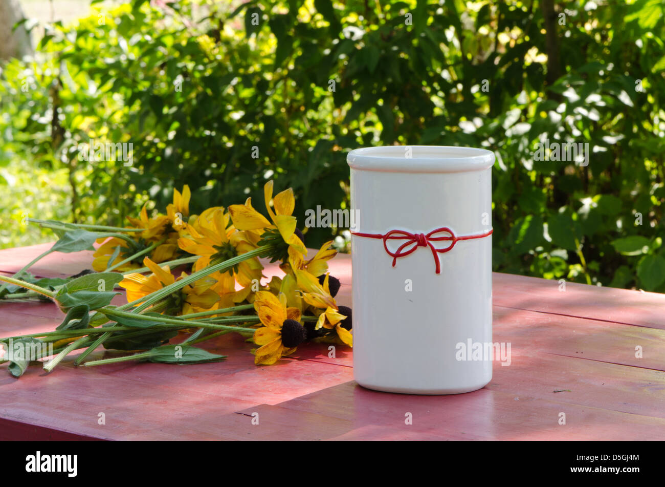 rudbekia flowers lie near white decorative beautiful vase on rural outdoor wooden table. Stock Photo