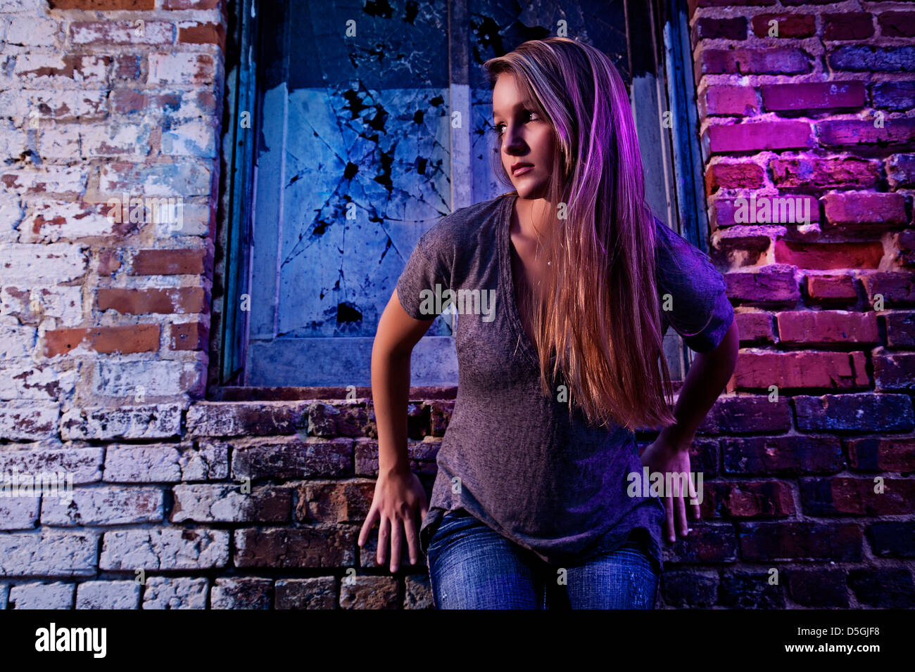 Teenage girl leaning against purple colored brick wall Stock Photo