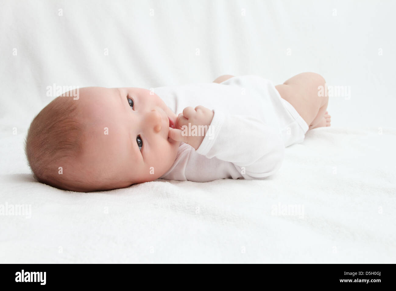 Beautiful baby on back on white bed Stock Photo