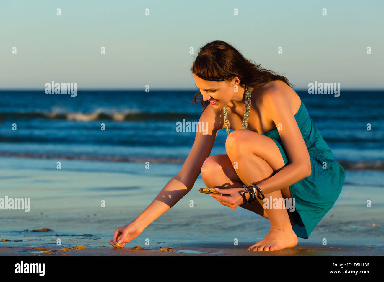 Woman looking for shells at the ocean beach in sunset Stock Photo