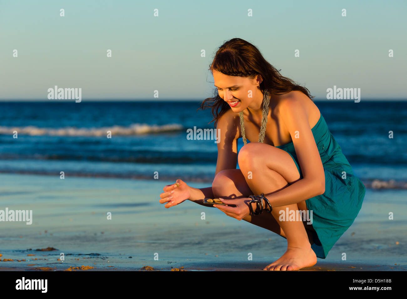 Woman looking for shells at the ocean beach in sunset Stock Photo