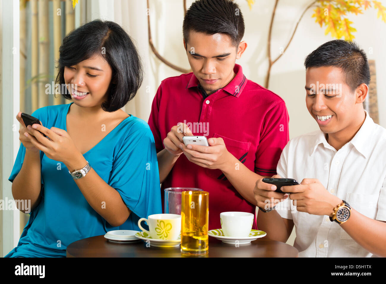 Asian people having fun together with mobile phone and drinking coffee or cocktail Stock Photo