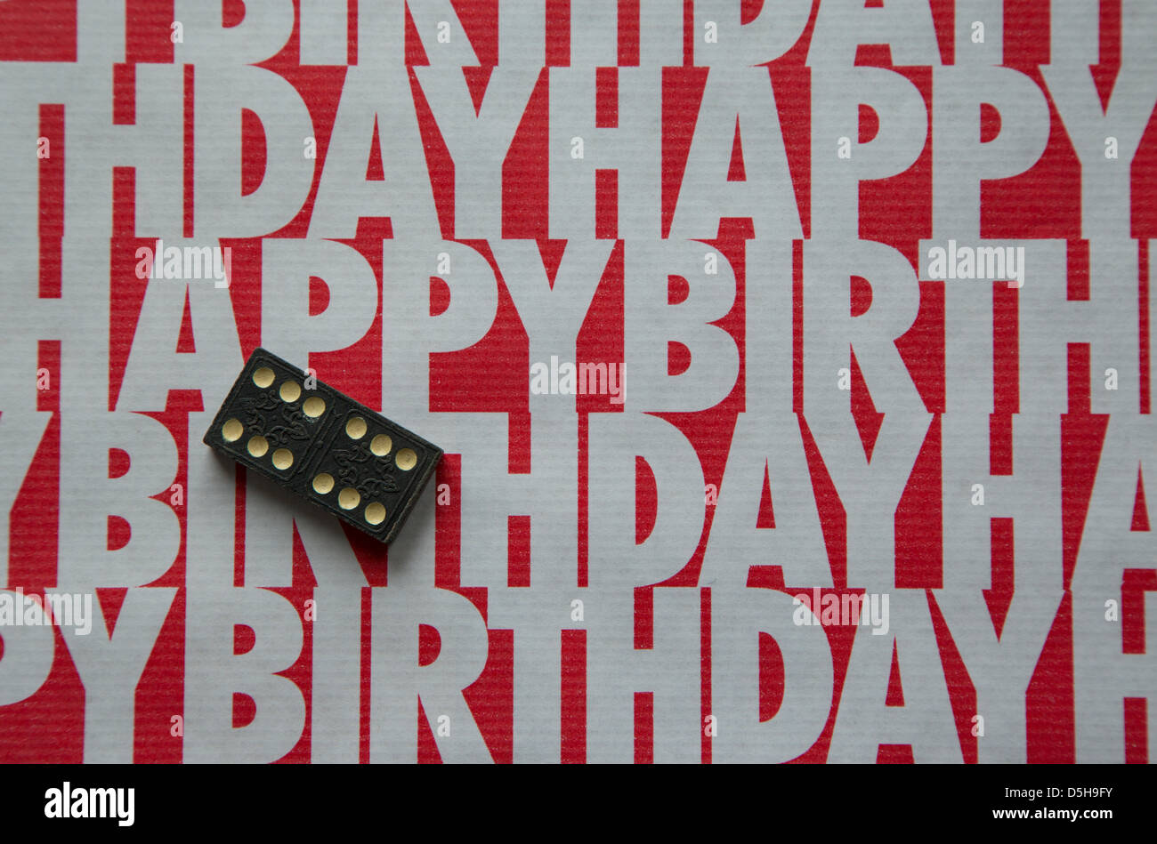 A shot of some 'happy birthday' wrapping paper in contrasting red and white colors, including a domino for contrast. Stock Photo