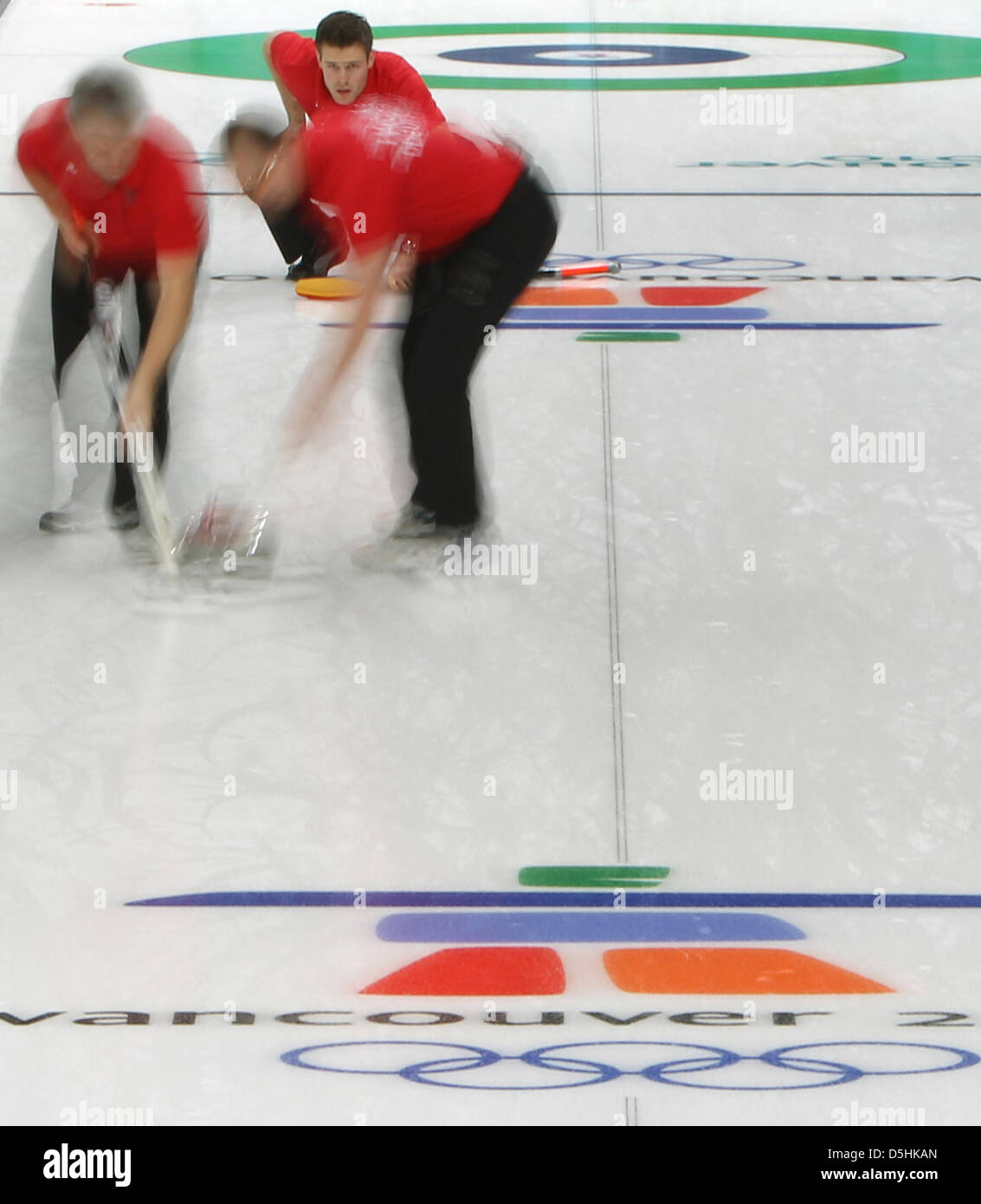 Andy Lang (M) of Germany releases his stone as Andreas Kempf (L) and Holger Hoehne guide it during Curling men's round robin session 3 at the Olympic Center during the Vancouver 2010 Olympic Games in Vancouver, Canada 17 February 2010. Germany's opponent was Sweden. Photo: Daniel Karmann Stock Photo