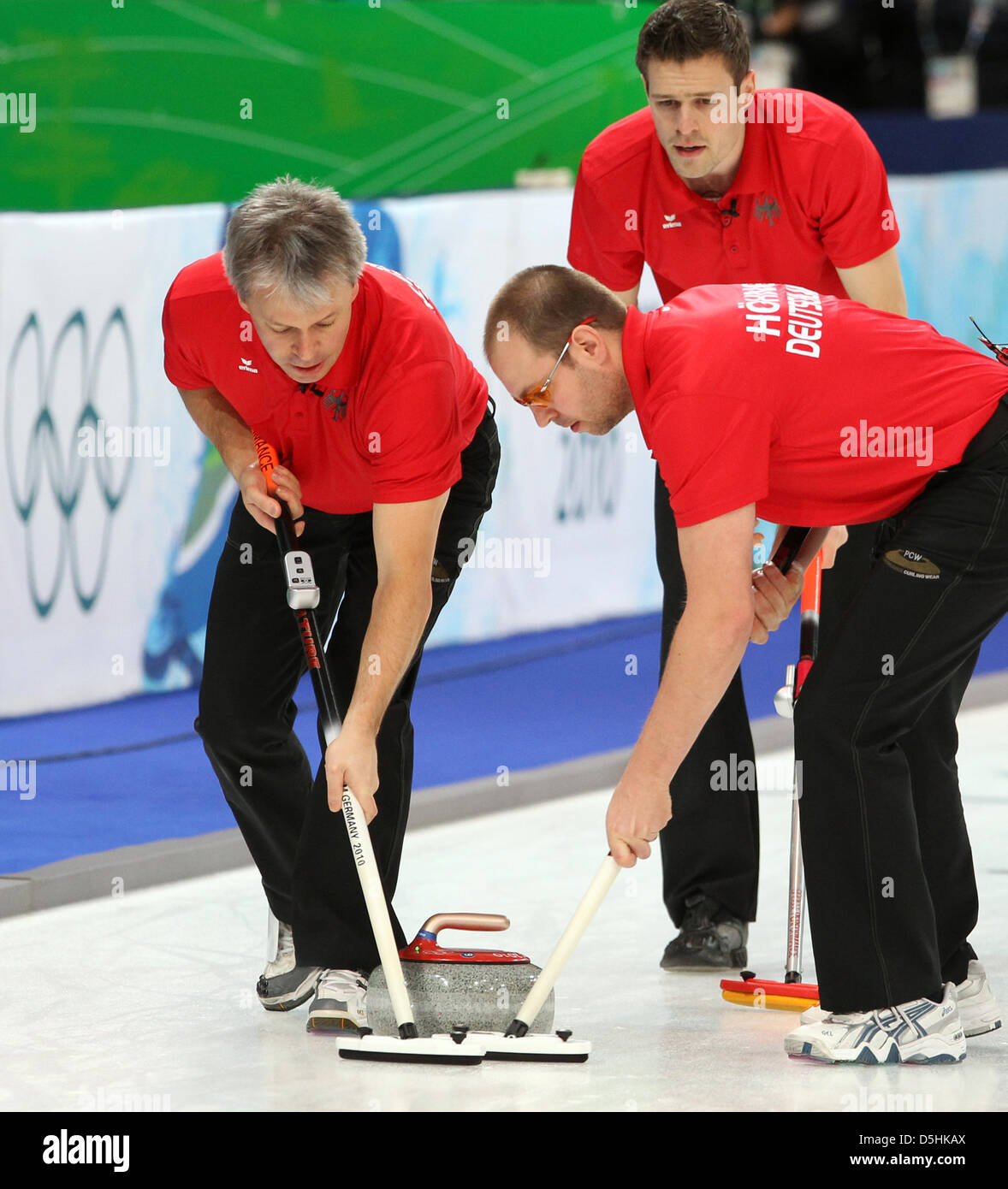 Andy Lang (R) of Germany releases his stone as Andreas Kempf (L) and Holger Hoehne guide it during Curling men's round robin session 3 at the Olympic Center during the Vancouver 2010 Olympic Games in Vancouver, Canada 17 February 2010. Germany's opponent was Sweden. Photo: Daniel Karmann Stock Photo