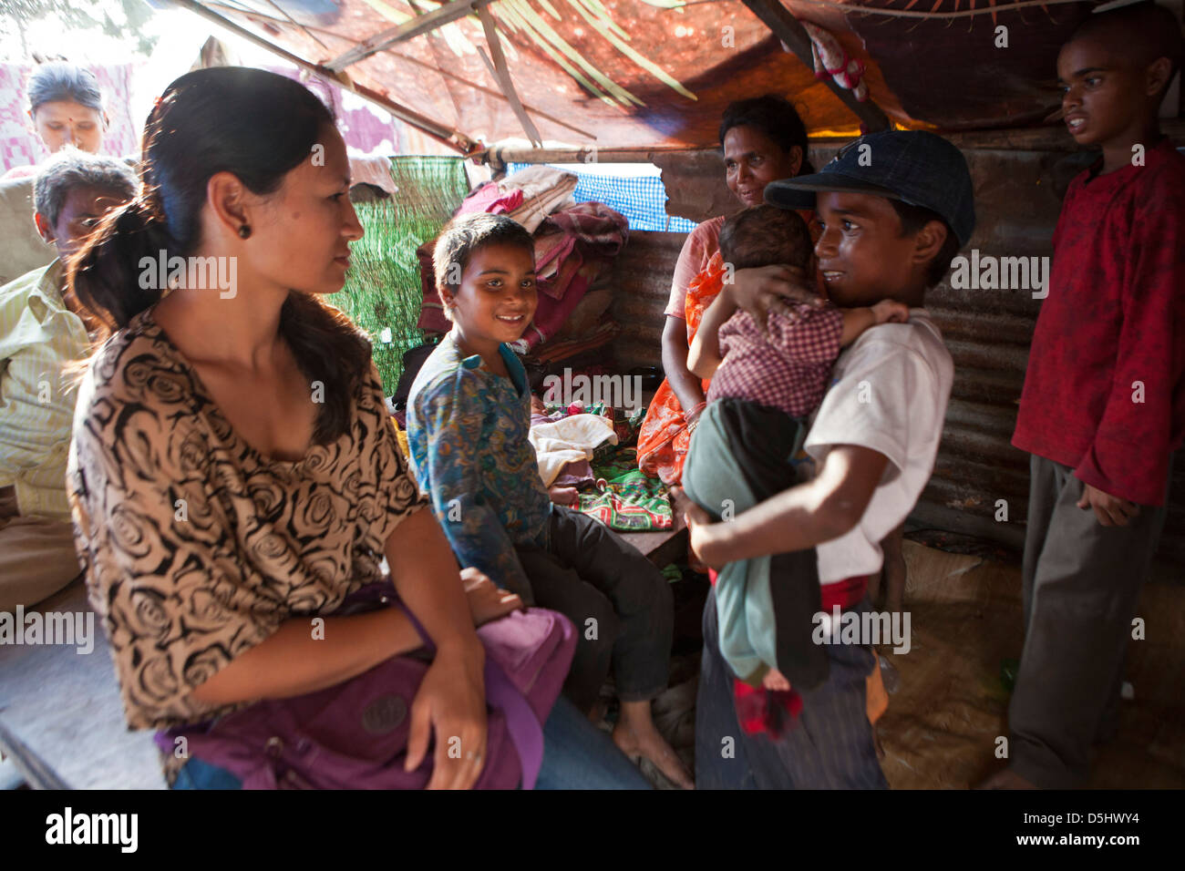 Nepalese boy holds one of his siblings as he talks to a charity visitor at home in slum in Kankeshori area of Kathmandu, Nepal. Stock Photo