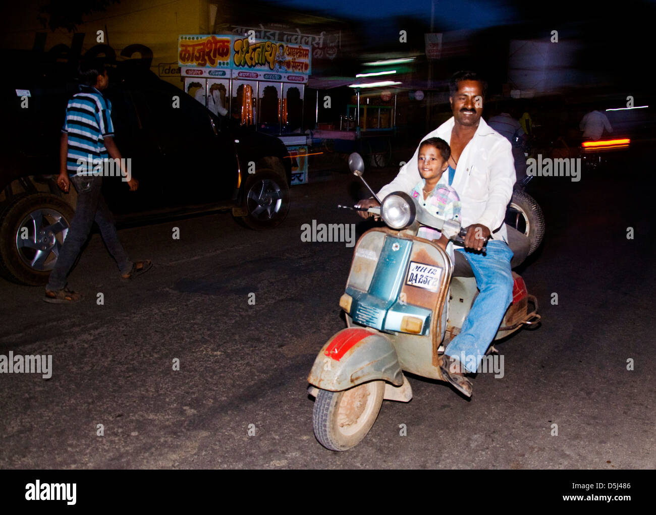 Indian man and boy on a motor scooter at night with no helmets on Stock  Photo - Alamy