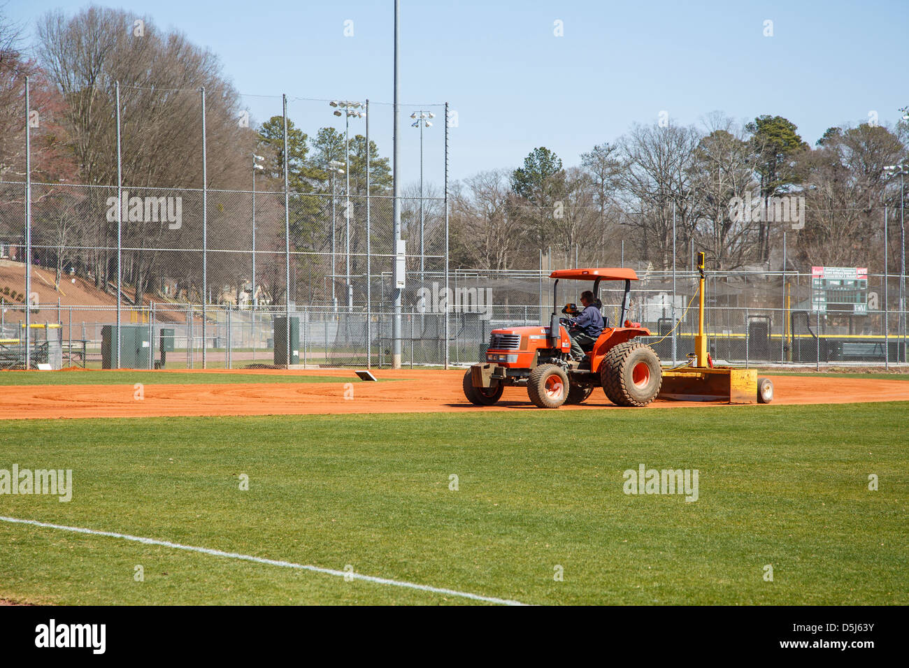 A man driving landscaping equipment across infield of little league baseball field in the spring Stock Photo