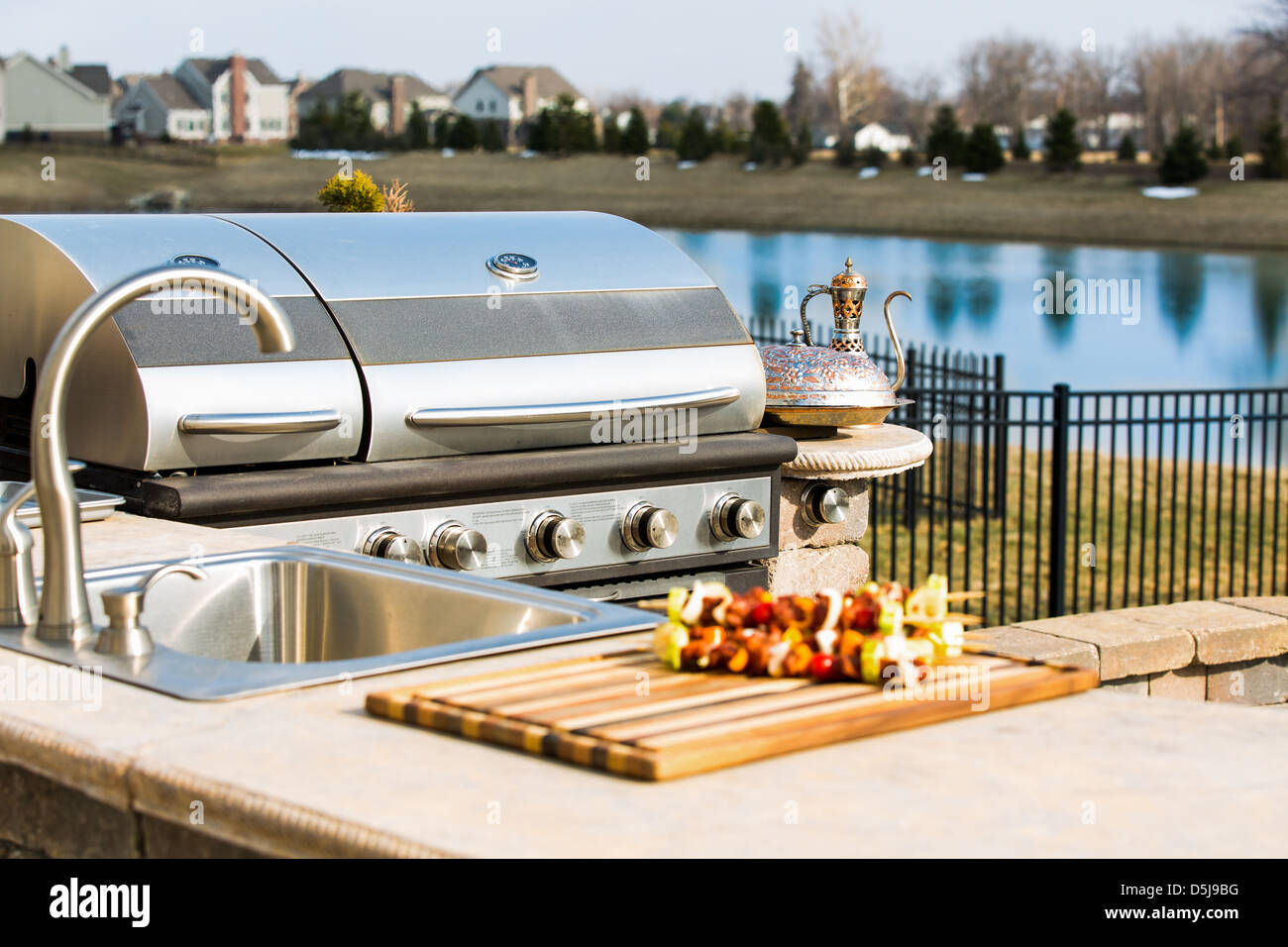 Bearbecue in outside kitchen along with sink and complimented with skewers and copper plate. Stock Photo