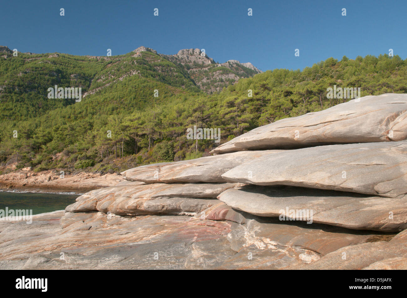 Greek island September Rocks beside Paradise Beach Mountains and thickly wooded slopes Stock Photo