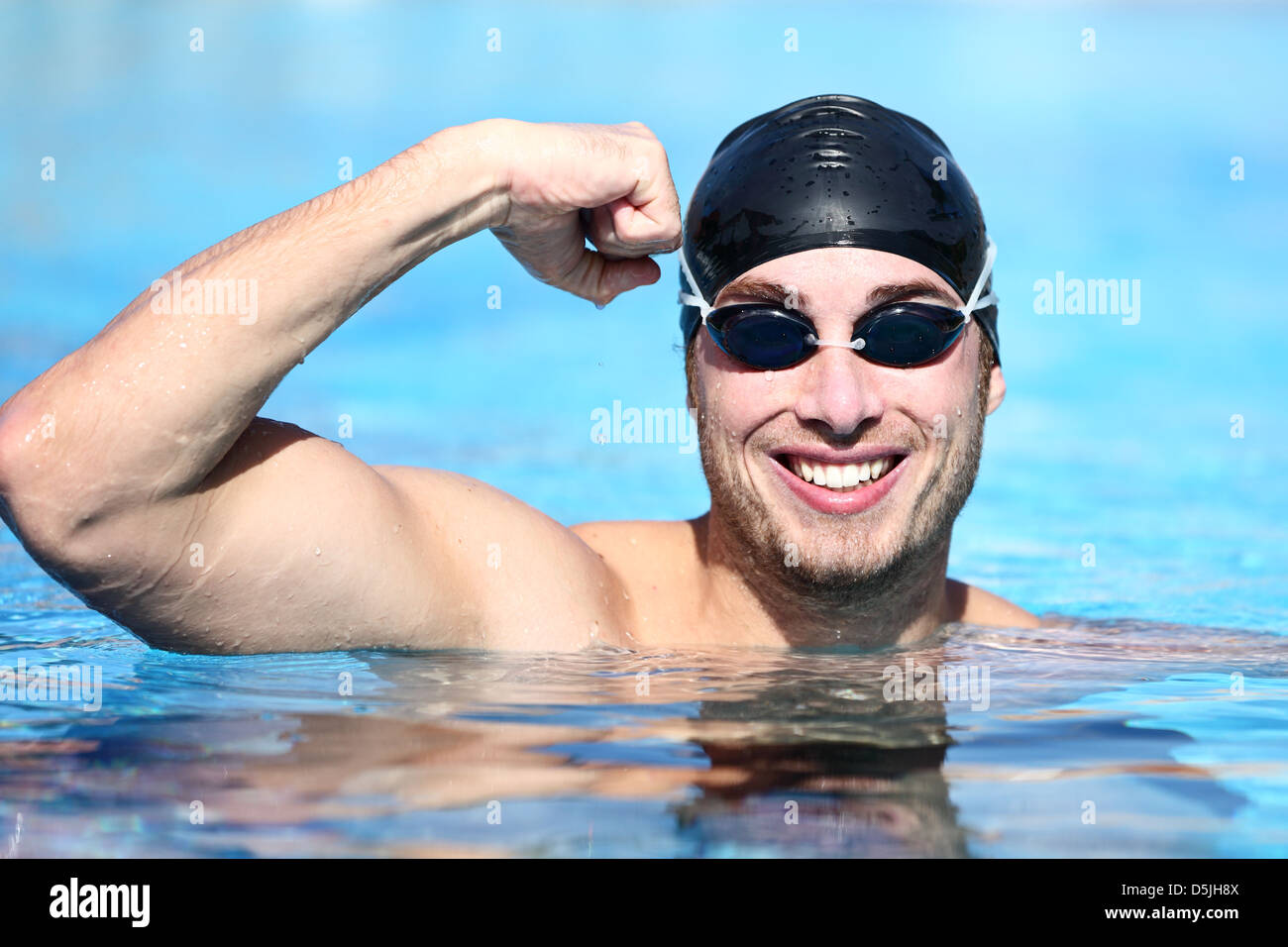 Happy Caucasian man wearing swim goggles and swimming cap celebrating victory in pool Stock
