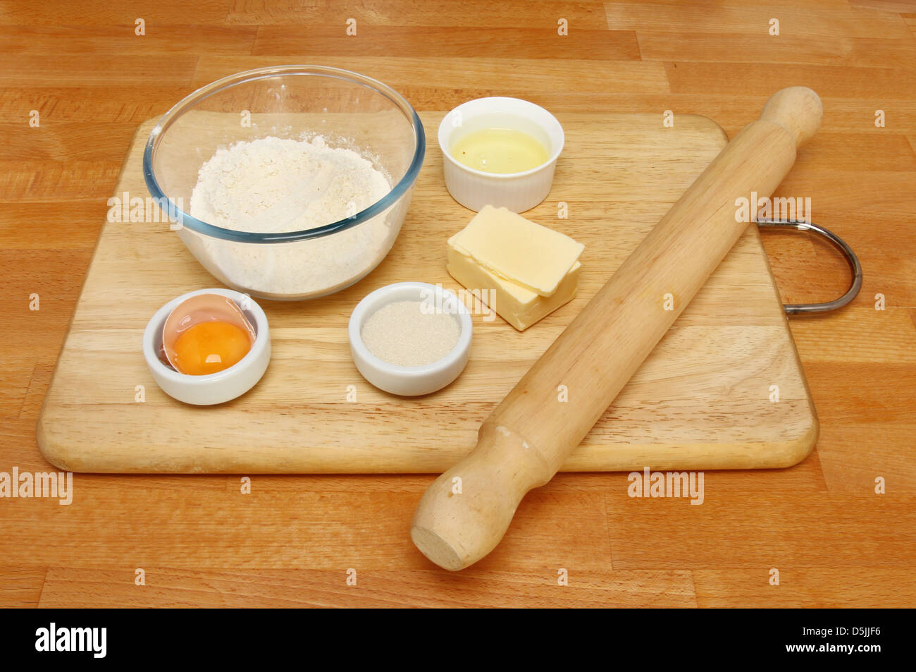 Pastry ingredients and rolling pin on a wooden board on a kitchen worktop Stock Photo